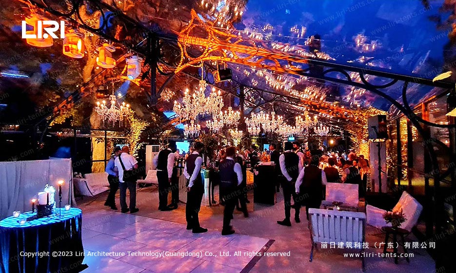 Orangery tent night party interior with chandeliers and cocktail guests